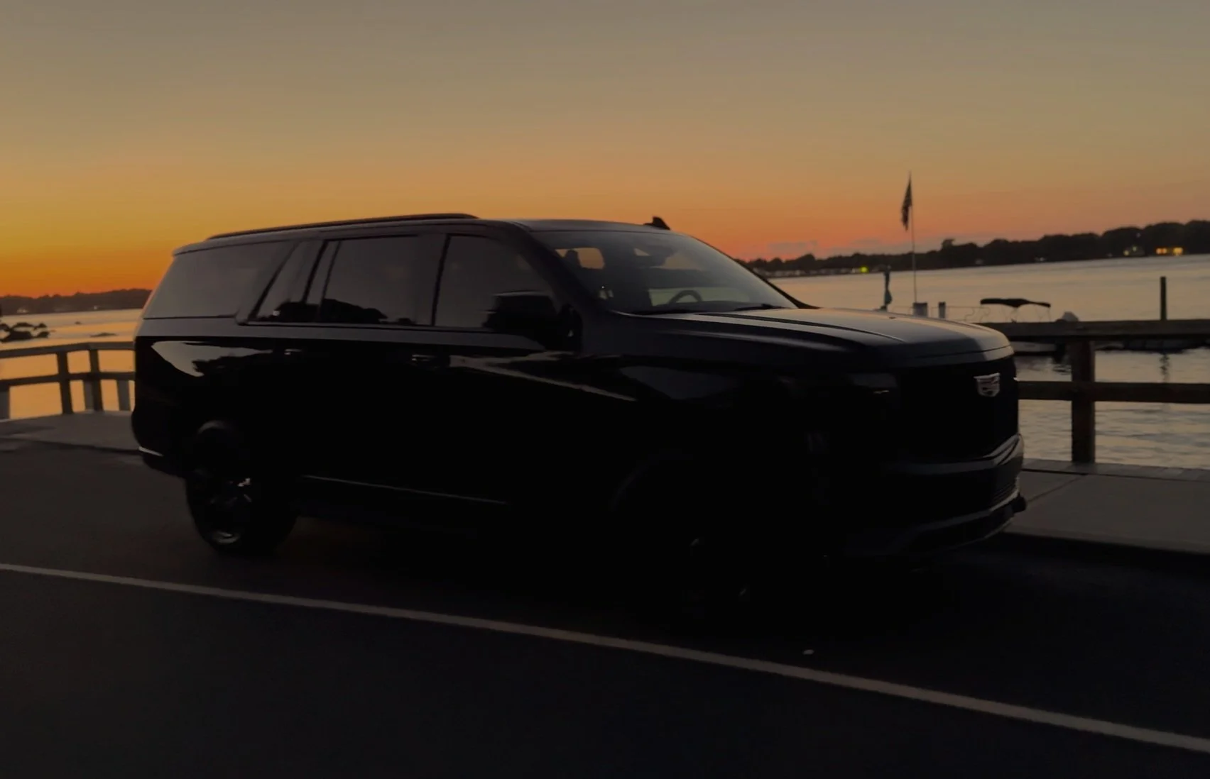 Black Cadillac Escalade beside the water at sunset